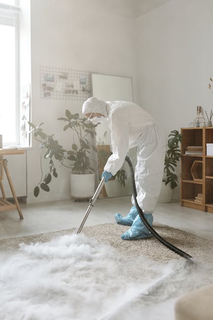A professional cleaner from Finchley Carpet Cleaners is performing deep surface cleaning on a beige carpet in a bright, minimalistic living room. The cleaner is wearing a full white protective suit, i
